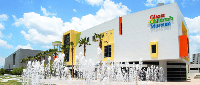 Exterior of Glazer Children's Museum with fountain in front, under a clear sky.