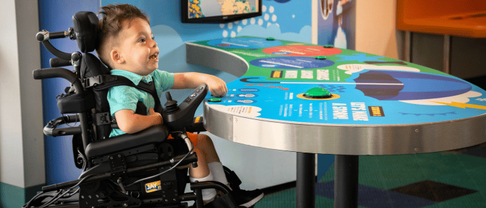 Child in a wheelchair at an interactive display table.