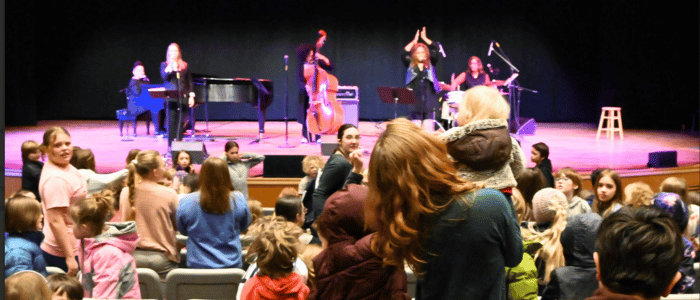 The Dennos Museum A lively music performance with a band on stage, while an engaged audience, including children and adults, enjoys the event.