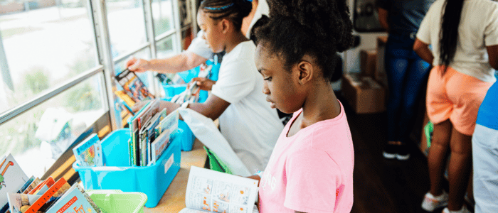 Juvenile Welfare Board of Pinellas County B (2) Children browsing and reading books in a bright room, with bins of books along the window.