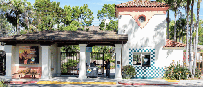 Santa Barbara Zoo (1) Entrance gate of a zoo or park with ticket booths, signage, and tropical landscaping on a sunny day.