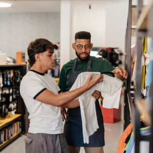 An employee assists another man with a shirt inside a store