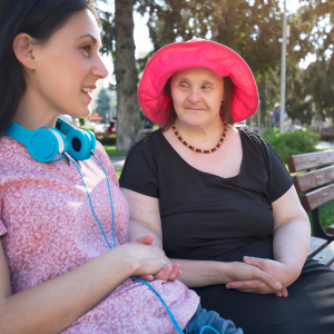 Two women sit outside on a park bench talking, one woman has Down syndrome