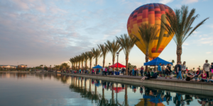 Lake with festival tents setup to the side with a hot air balloon in the background